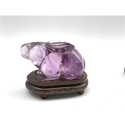 Oriental amethyst glass rabbit on a wooden stand W9cm and an early 20th century carved ivory figure of a lion on wooden stand W11cm 