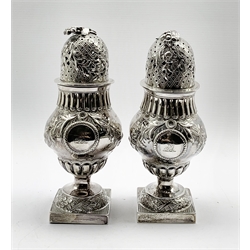 Pair of vase shape silver sugar casters, the two cartouches engraved with a crest and monogram, embossed with trailing flowers and with floral finials on square bases H19cm Sheffield 1903/4 Maker James Dixon & Sons 19oz