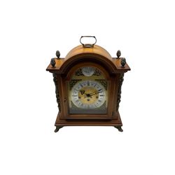 A contemporary German replica of an 18th century style bracket clock in a light mahogany break arch case, with carrying handle, finials, silk backed side frets on a shallow moulded plinth raised on four paw feet, with a brass dial, silvered chapter ring, brass spandrels and steel pierced hands, Schneckenbecher eight day three train Westminster chime movement with a floating balance escapement and strike /silent facility. With key.