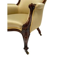 Victorian walnut armchair, curved back with moulded frame, upholstered in pale yellow fabric, scroll carved arm terminals and shaped uprights, cabriole supports on brass castors, sprung seat 