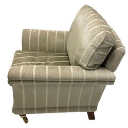 Traditional shaped armchair with scrolled arms, upholstered in pale sage striped fabric, raised on tapered supports with brass cups and castors