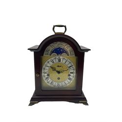 Compact late 20th century German Westminster chiming mantle clock in a break arch mahogany effect case with a brass carrying handle, conforming glazed door, etched brass dial with a silvered “Dutch” chapter ring, Roman numerals and minute track, steel serpentine hands with a working moon phase feature, Hermle 8-day three-train spring driven movement with a floating balance, chiming the quarters and hours on 5 gong rods.


