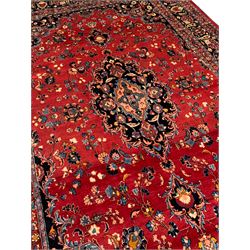 Persian Kashan crimson ground carpet, the central indigo pole medallion surrounded by sparsely placed bouquets interconnected with foliate branches, the guarded border with repeating palmette and Boteh motifs with interwoven scrolling patterns