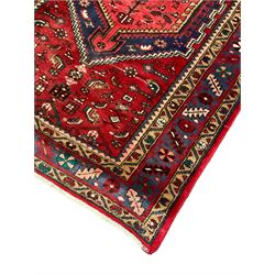 Persian Hamadan crimson ground rug, the field with a central indigo elongated lozenge containing secondary geometric patterns, surrounded by stylised plant and bird motifs, the multi-guarded border with repeating geometric designs and flowerheads