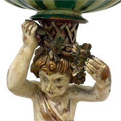Italian design polychrome carved wood figure depicting Putto holding a shell aloft, shaped shell form basin resting on the head of the putto's coiffure, holding foliage festoon, the raised knee rests upon C-scroll decorated with foliage, berries and flutes, waisted circular form base in the form of shells with moulded upper edge over carved S-scrolls, on four C-scrolled foliage feet 