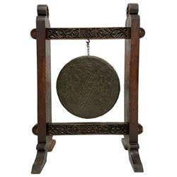 Late 19th century carved oak frame gong on stand, the pegged frame carved with scrolling foliage and flower heads, tooled bronze hanging gong, the lower pegged rail dated '1880', on splayed feet