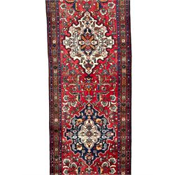 Persian Hamadan red ground runner, the field decorated with triple floral design medallions surrounded by trailing stylised plant motifs, the border decorated with repeating flower heads