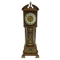 An Edwardian oak miniature longcase clock with a broken pediment and central brass finial, hood with applied brass spandrels supported on four reeded brass columns with Corinthian capitals, trunk with scrolled brass decoration on a corresponding stepped plinth raised on four ogee bracket feet, eight-day French timepiece movement with a later lever platform escapement, dial comprising a 3-1/4” enamel chapter ring with Arabic numerals and minute track, recessed applied decorative scroll work to the dial center, steel spade hands within a brass bezel and flat bevelled glass, rear wound and set.
With key.  
