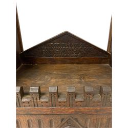 Large late 19th to early 20th century oak cabinet in the form of the York Minster western front, depicting the two towers with crocketed pinnacles over carved tracery work windows, fitted with a combination of compartments enclosed by small doors disguised as windows, central portal door and flanking side doors, sloped arched pediment inscribed 'West front of York Minster as seen from the ancient ramparts', decorated with pointed niches with carved figures 