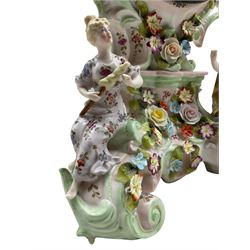 Mid-19th century continental porcelain mantle clock in the Meissen Rococo style decorated with encrusted flowers throughout and reclining figures depicting two lovers encouraged by Cupid, French twin barrel eight-day countwheel movement striking the hours and half hours on a bell, two-piece white enamel dial with upright Arabic numerals and minute markers, fleur de lis steel hands enclosed within a cast brass bezel with a flat bevelled glass. No pendulum or key