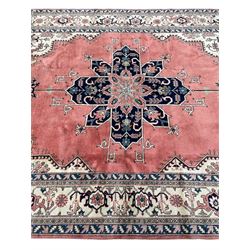 Persian Heriz pale peach ground rug, the plain field with blue geometric medallion within stepped angular field, the spandrels and border decorated with repeating stylised motifs