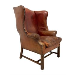 Georgian design mahogany framed wingback armchair, high back shaped cresting rail over down-scrolled arms, upholstered in tan leather with studwork border and loose seat cushion, raised on moulded square supports united by H-stretcher