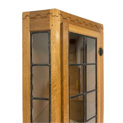 Mouseman - oak floor-standing corner cabinet, arcade carved cresting over lead glazed single door and uprights, the lower cupboard enclosed by panelled door with wrought metal fixtures, carved with mouse signature, on skirted base, by the workshop of Robert Thompson, Kilburn 