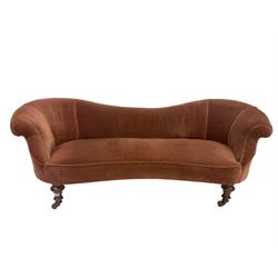 Late 19th century low-back settee, serpentine back and front, upholstered in velvet fabric with sprung seat and raised on turned feet with brass castors