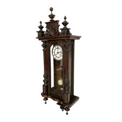 Late 19th century German 8-day striking wall clock in a mahogany case -  pediment with carved decoration and turned finials, fully glazed door flanked by carved pilasters displaying a gridiron pendulum and beat plate, two part enamel dial with gothic pierced hands and spun brass bezel, 
movement striking the hours and half hours on a coiled gong.