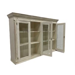 Painted pine wall cabinet, projecting cornice with dentil derail, fitted with four glazed doors enclosing four shelves, flanked by reeded pilasters, in cream finish