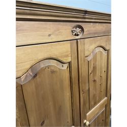 Pine double wardrobe, the projecting cornice over carved frieze and two cupboard doors opening to reveal interior fitted for hanging and two drawers, raised on a plinth base 