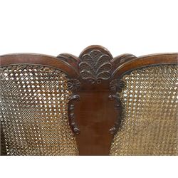 Early 20th century walnut bergère two seat sofa, the back and arms with double cane panels, the shaped back carved and applied with foliate and shell decoration and stylised palms, upholstered in latte corduroy fabric with sprung seat and loose cushions, raised on cabriole supports with ball and claw feet 