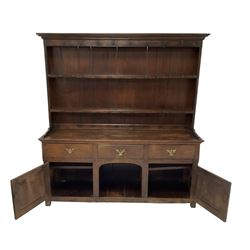 George III oak dresser, projecting cavetto cornice over two-tier plate rack and hooks, fitted with three drawers over two panelled cupboard doors flanking central recess, raised on stile feet