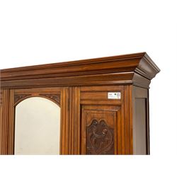 Late Victorian walnut double wardrobe, projecting cornice over arched bevelled mirror door flanked by foliate carved panels, enclosing hanging rail and coat hooks, single drawer to base