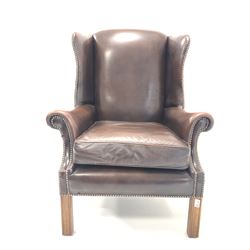 George III style wing back armchair, upholstered in studded brown leather, raised on square moulded front supports W79cm