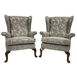 Pair of wingback armchairs upholstered in light grey fabric, raised on cabriole supports 