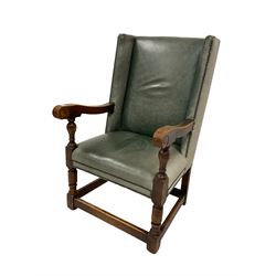 Early 20th century oak framed wing back armchair, upholstered in studded leather with sprung seat, the arms terminating in carved scrolls with turned front supports 
