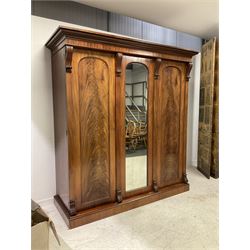 Late 19th century mahogany triple wardrobe, the projecting cornice over banded frieze, the central door with arched full length mirror flanked by two figured panelled doors, the uprights topped with reeded and scrolled corbels decorated with acanthus leaves, the interior fitted with coat hooks,  two hanging rails and two drawers, raised on plinth base 
Provenance: property of a gentleman