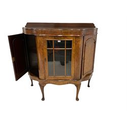 Early 20th century figured walnut serpentine side cabinet, shaped top with raised back, fitted with centre astragal glazed door enclosing two glass shelves, flanked by two arch panelled cupboards, raised on cabriole supports with pad feet