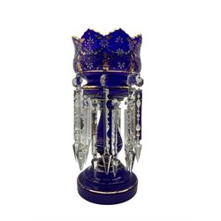 19th/ early 20th century blue glass table lustre decorated with gilt and white enamel flowerheads, the bowl and knopped stem suspending sixteen prismatic drops H37.5cm, displayed within a clear glass dome on oak and beech stepped base H53cm overall