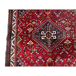 Persian Shiraz red ground rug, the central geometric medallion lozenge and matching spandrels decorated with central Koçboynuzu motifs, the field with all-over stylised plant symbols, guarded ivory border with repeating foliate patterns