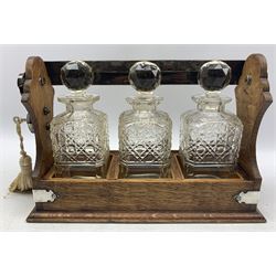 Edwardian oak three bottle tantalus with plated mounts, fitted with three square spirit decanters W35cm 