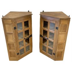 'Rabbitman' pair panelled oak wall hanging corner cabinets, enclosed by astragal glazed doors, ironwork hinges and strap latches, each fitted with three shelves to interior, both carved with rabbit signature, with wall brackets, by Peter Heap of Wetwang, W67cm, H96cm, D46cm