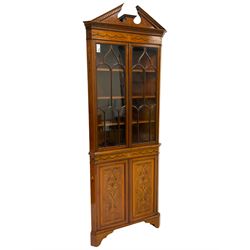 Edwardian inlaid mahogany and satinwood corner cabinet, the upper section with sloped broken dentil pediment, the frieze inlaid with central urn with extending linen swags, enclosed by two astragal glazed doors, the lower section with matching linen swag inlaid frieze over double cupboard, the panelled doors inlaid with scrolling leafy branches and flower heads, on bracket feet