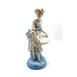 Late 19th century French standing figure of a girl holding a large basket on a blue base, possibly Charenton H39cm