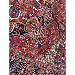 Persian Heriz crimson ground carpet, the field decorated with a central floral medallion surrounded by geometric stylised plant motifs with contrasting ivory spandrels, the multi-band border with repeating foliate patterns