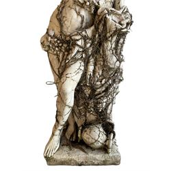 Mid-20th century Classical design cast stone figure of Bacchus or Dionysus, leaning against a tree stump semi-nude draped in grapes and trailing vine branches, holding a cup and wine vessel, the figure covered in trailing branches 