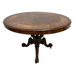 Victorian inlaid walnut breakfast table, figured tilt-top with quarter-matched veneers, inlaid with trailing foliate decoration within stringing, open pedestal base with shaped and moulded uprights and central turned supports, carved with scrolls and foliage, three shaped splayed supports with scroll terminals, on brass and ceramic castors