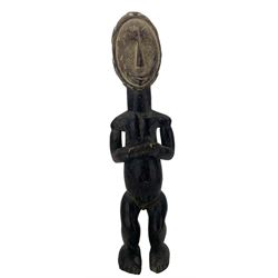 West African carved hardwood male tribal figure in crouching pose, oval face with incised and geometric design H62cm