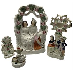 Four pieces of 19th century Staffordshire pottery to include a large flatback depicting newly weds seated under a grapevine arch; a figural pocketwatch holder; a flatback depicting a couple with clock and a spill vase in the form of a swan
