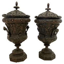 Pair of mid-to-late 20th century Baroque Revival carved wood Campana-shaped urns, the lid with pineapple finial over scrolled acanthus leaf, oval flower head carved band over the main body decorated with festival scenes, the underbelly carved with green man masks and scrolling foliate, the handles in the form of scrolled leafage, the foot carved with an interlaced band and beads over the foliate carved circular platform, octagonal base with foliate edge and scroll carvings to each panel 