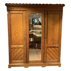 Late Victorian pitch pine triple wardrobe, projecting cornice over central mirror glazed doors and flanking panelled doors, the two left-hand doors enclosing four linen slides over two short and two long drawers, on plinth base