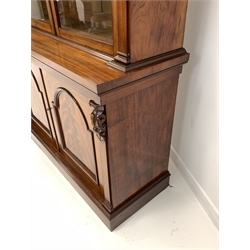 Victorian mahogany bookcase, projecting cornice over leaf and scroll carved corbels and two arched glazed doors enclosing four adjustable shelves, two panelled cupboards under enclosing a fixed shelf, on plinth base 