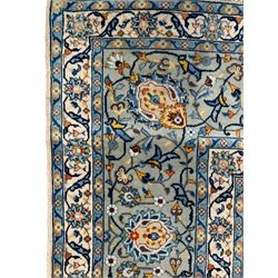 Persian Kashan ivory ground carpet, trailing and interlaced leafy branches interspersed with stylised peony and flowerhead motifs, the border with similar scrolling pattern within guard bands