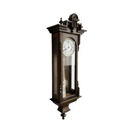 German - 20th century 8-day spring driven wall clock in a 19th century styled mahogany case, case with a carved pediment, finials and ogee base, fully glazed door with a two part enamel dial, Roman numerals and gridiron pendulum, Hermle twin train striking movement, sounding the hours and half hours on a gong. With key.