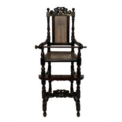 Victorian style stained beech child's high chair, scroll carved and pierced cresting rail over cane work back and seat, turned upright supports and moulded sweeping arms, on turned supports with scroll carved lower stretcher