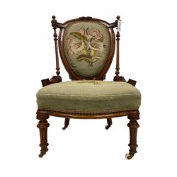Victorian walnut nursing chair, the cresting rail carved with central foliate decoration and framing scalloped detail, the backrest flanked by turned and fluted column supports with roundel carved capitals, the back and sprung seat upholstered in floral needlework fabric, raised on turned and fluted supports terminating in brass and ceramic castors