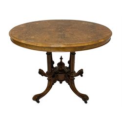 Victorian inlaid walnut centre table, the quarter-match veneer oval top with boxwood and ebony stringing and foliate inlay, raised on a cluster column base with fluted and lobe carved pilasters surrounding a central finial, the platford carved with scrolls and foliate decoration, terminating in splayed cabriole supports with brass and ceramic castors