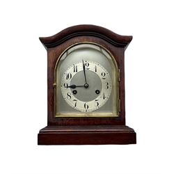 A Juhngans eight-day mantle clock in a mahogany case with a serpentine top striking the hours and half hours on a coiled gong, with a silvered dial and separate chapter ring, Arabic numerals, minute track and steel spade hands, arched topped glass door with a brass surround. No pendulum. 

