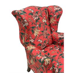 Late 19th to early 20th century wingback armchair, upholstered in 'Givenchy for Fabriyaz' fabric, pink ground and decorated with trailing floral pattern, upholstered seat cushion and sprung seat, on foliage carved ball and claw feet 